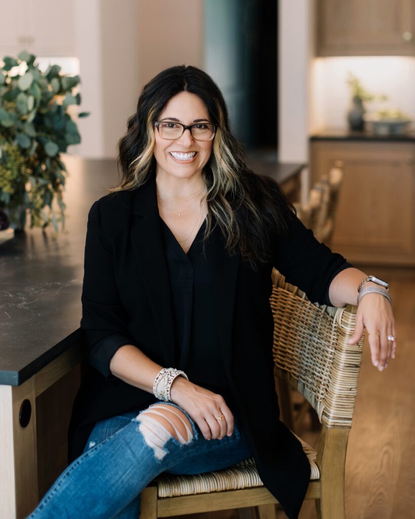 Angelique Baez - Interior Designer - is seated in a chair in front of a desk for a headshot